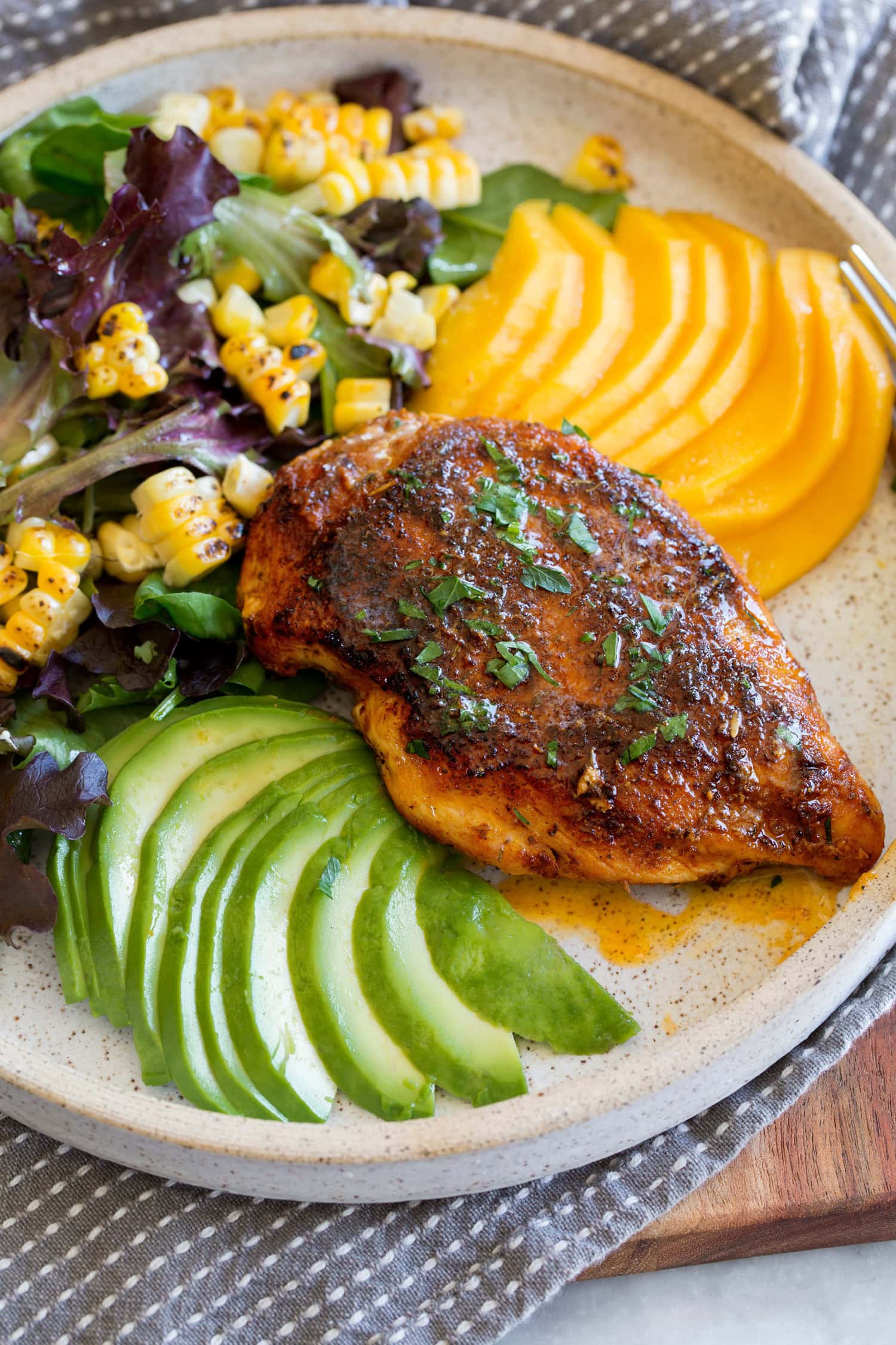 Blackened chicken breasts with serving suggestion of corn salad, mango and avocado.