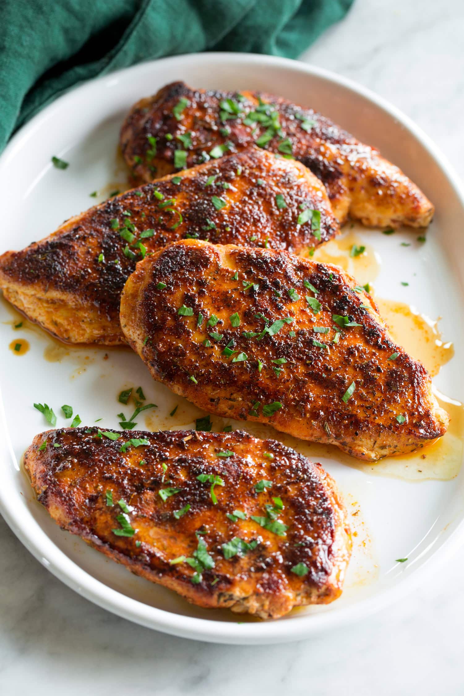 Blackened chicken breasts with butter and parsley garnish.