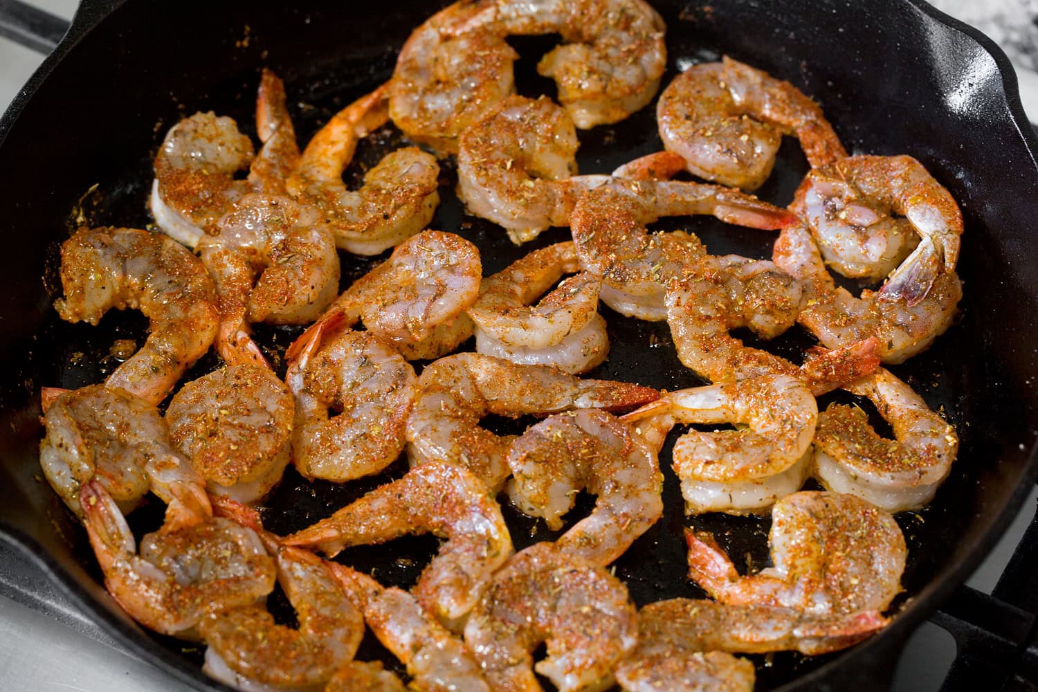 Blackened shrimp shown cooking in a cast iron skillet on the first side.