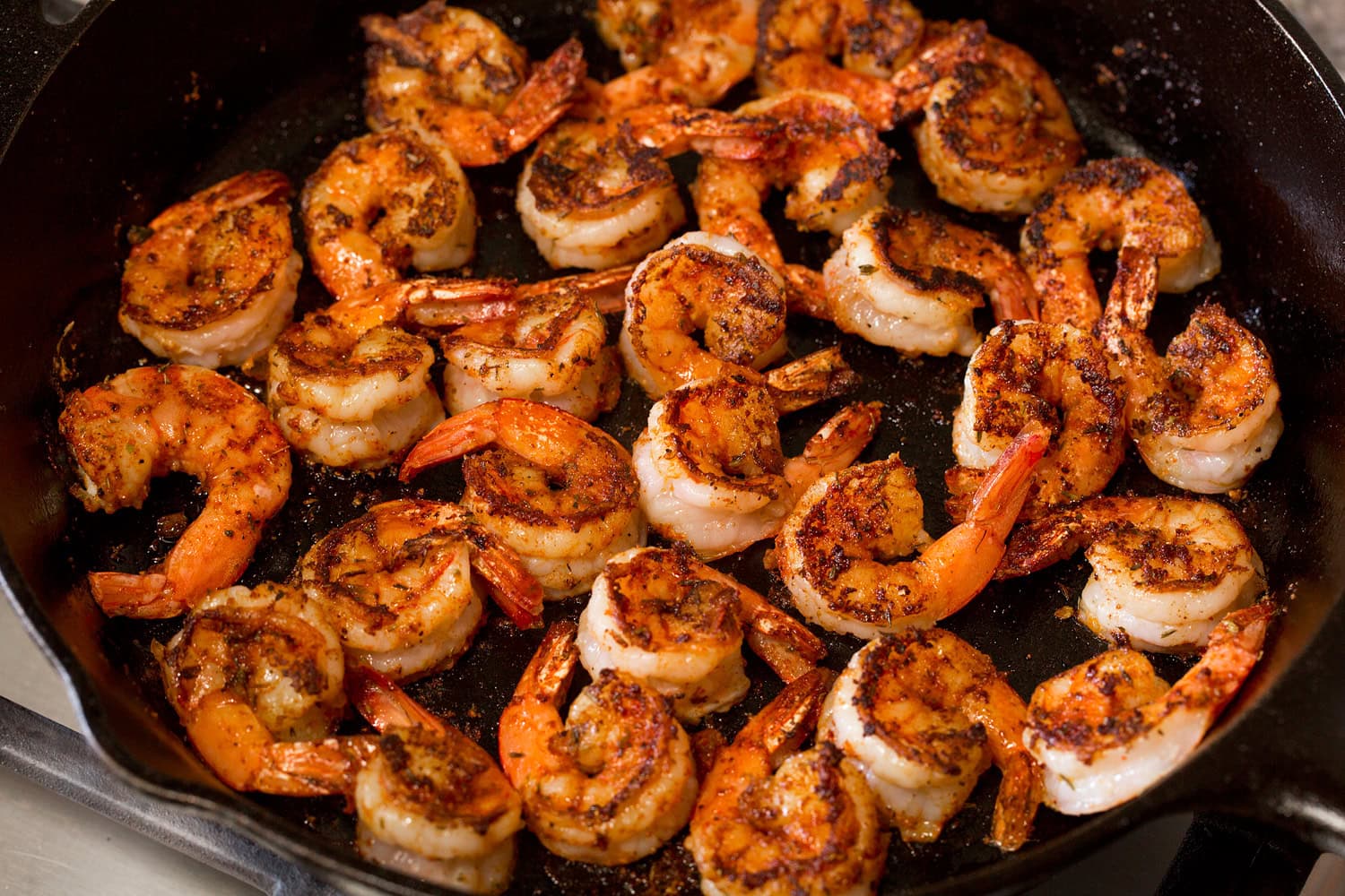 Blackened shrimp shown cooked through in a cast iron skillet on second side.