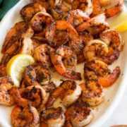 Seasoned blackened shrimp on a white serving platter with a green cloth to the side.
