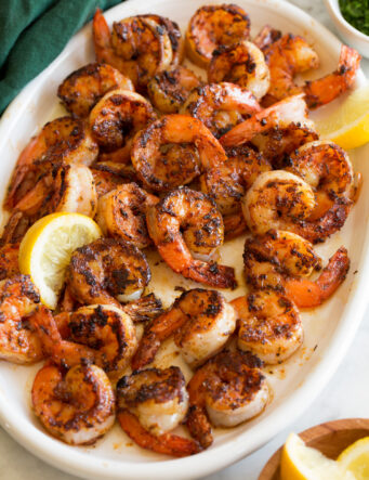 Seasoned blackened shrimp on a white serving platter with a green cloth to the side.