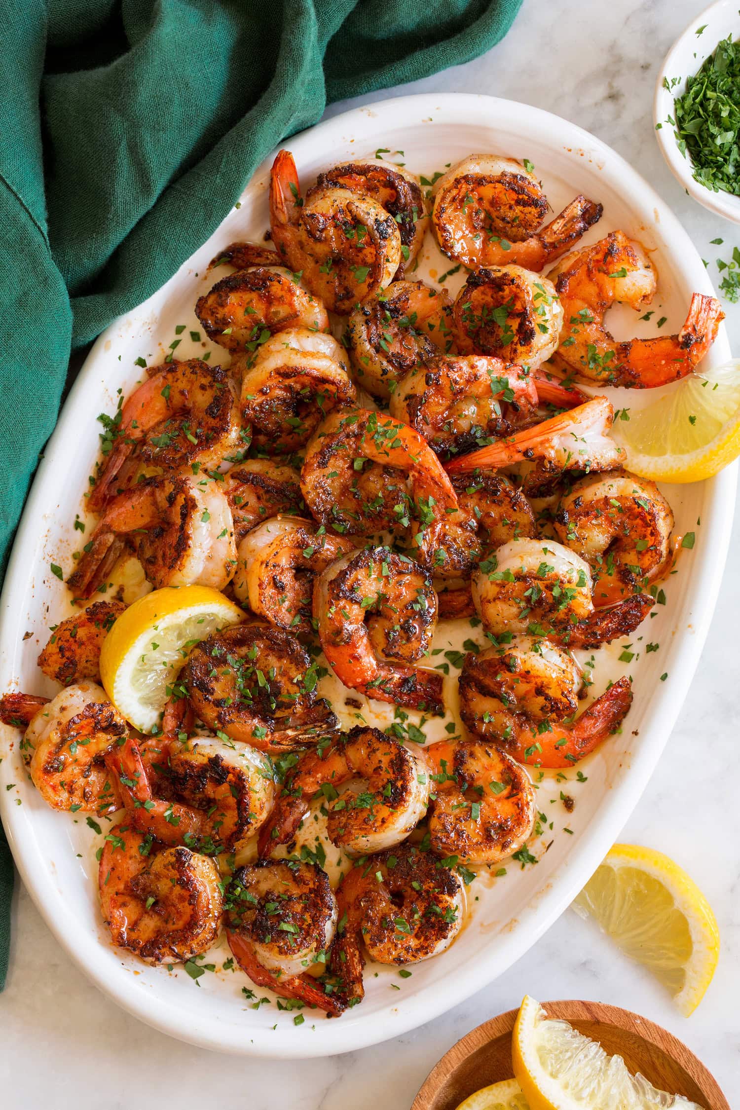 Blackened shrimp garnished with parsley shown on a white oval platter with lemon slices.