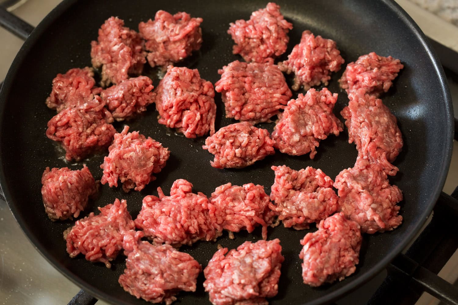Raw ground beef added to a dark skillet in chunks.