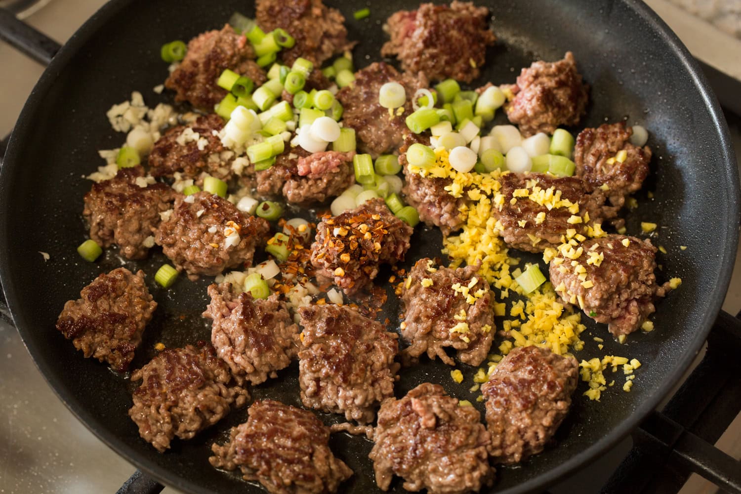 Ground beef shown browned on one side with green onions, garlic and ginger added.