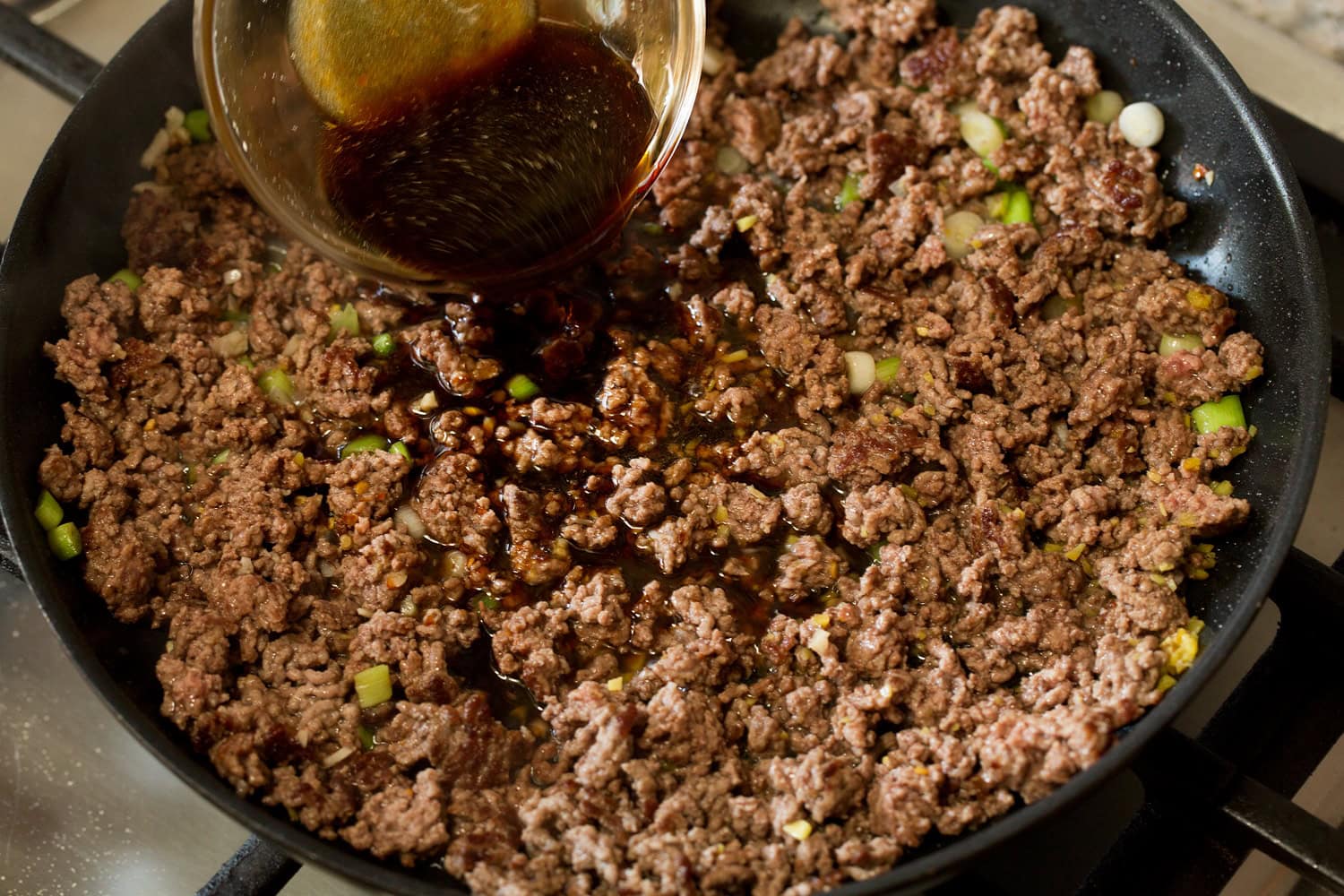 Crumbled browned beef with soy sauce mixture being added.