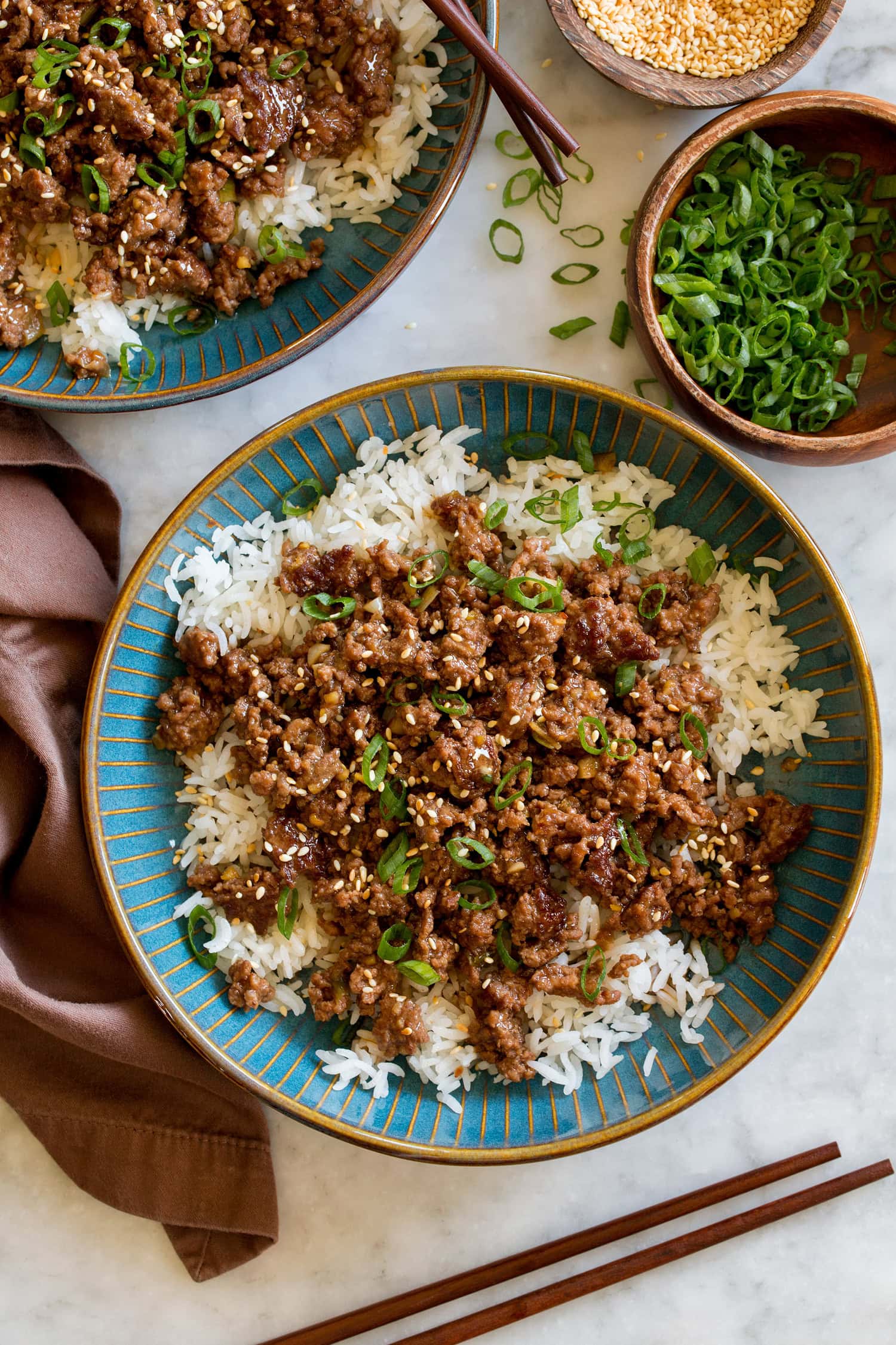 Korean beef in a blue bowl with white rice and green onions. Shown from overhead.
