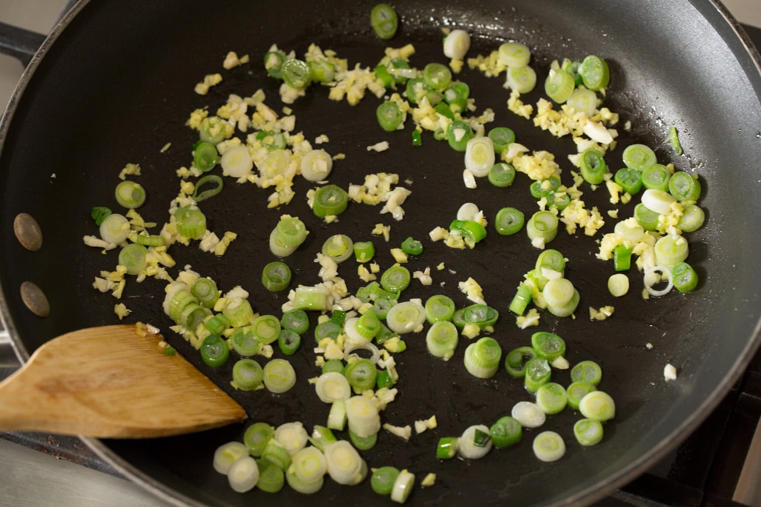 Green onions, garlic and ginger being sauteed in a skillet.