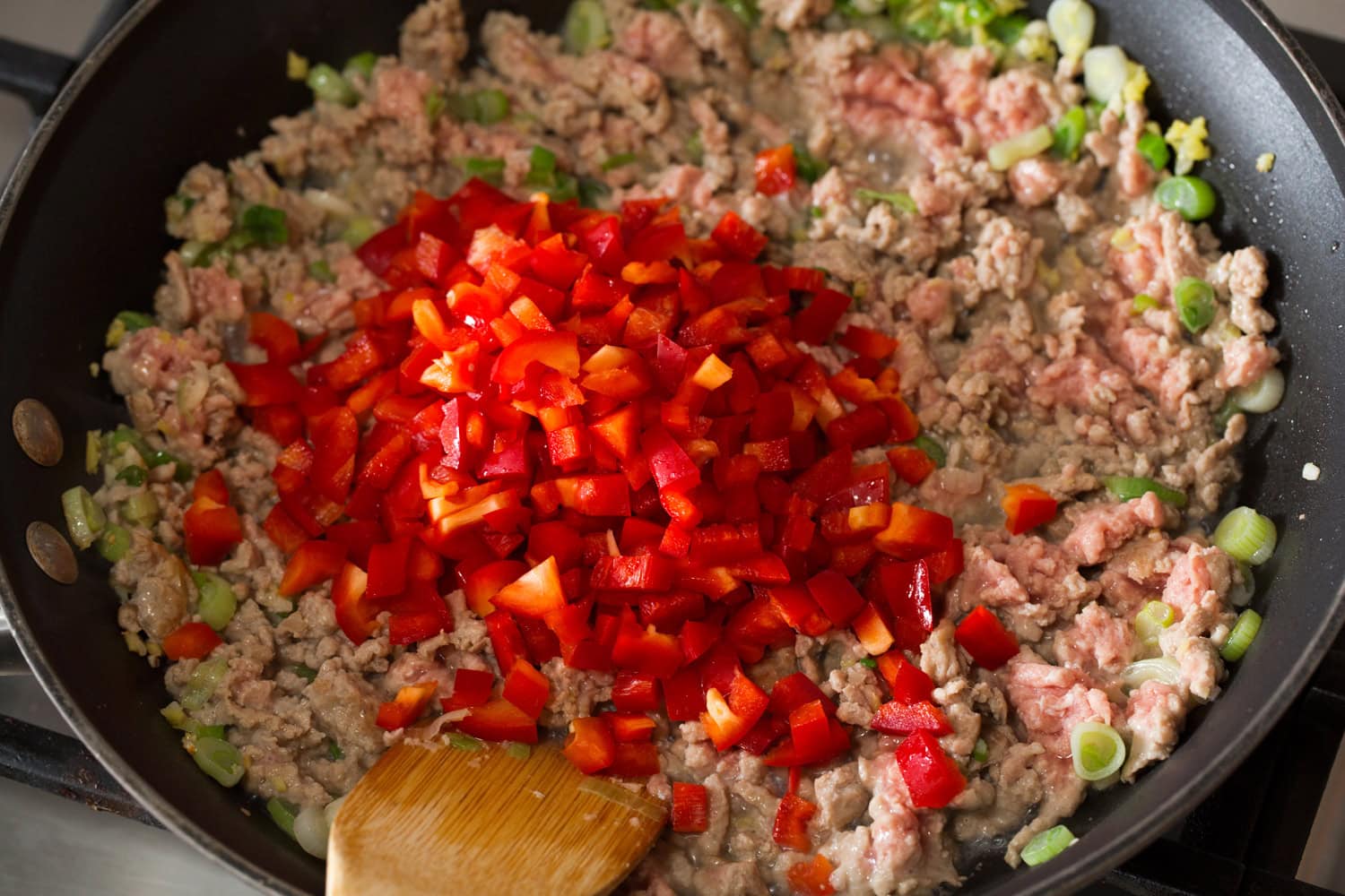 Chopped bell peppers being added to the ground meat in the skillet.