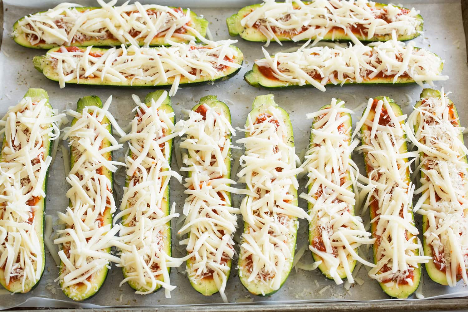 Zucchini pizza boats with shredded cheese on top.