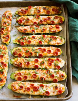Zucchini Pizza Boats on a large baking sheet with a green cloth to the side.
