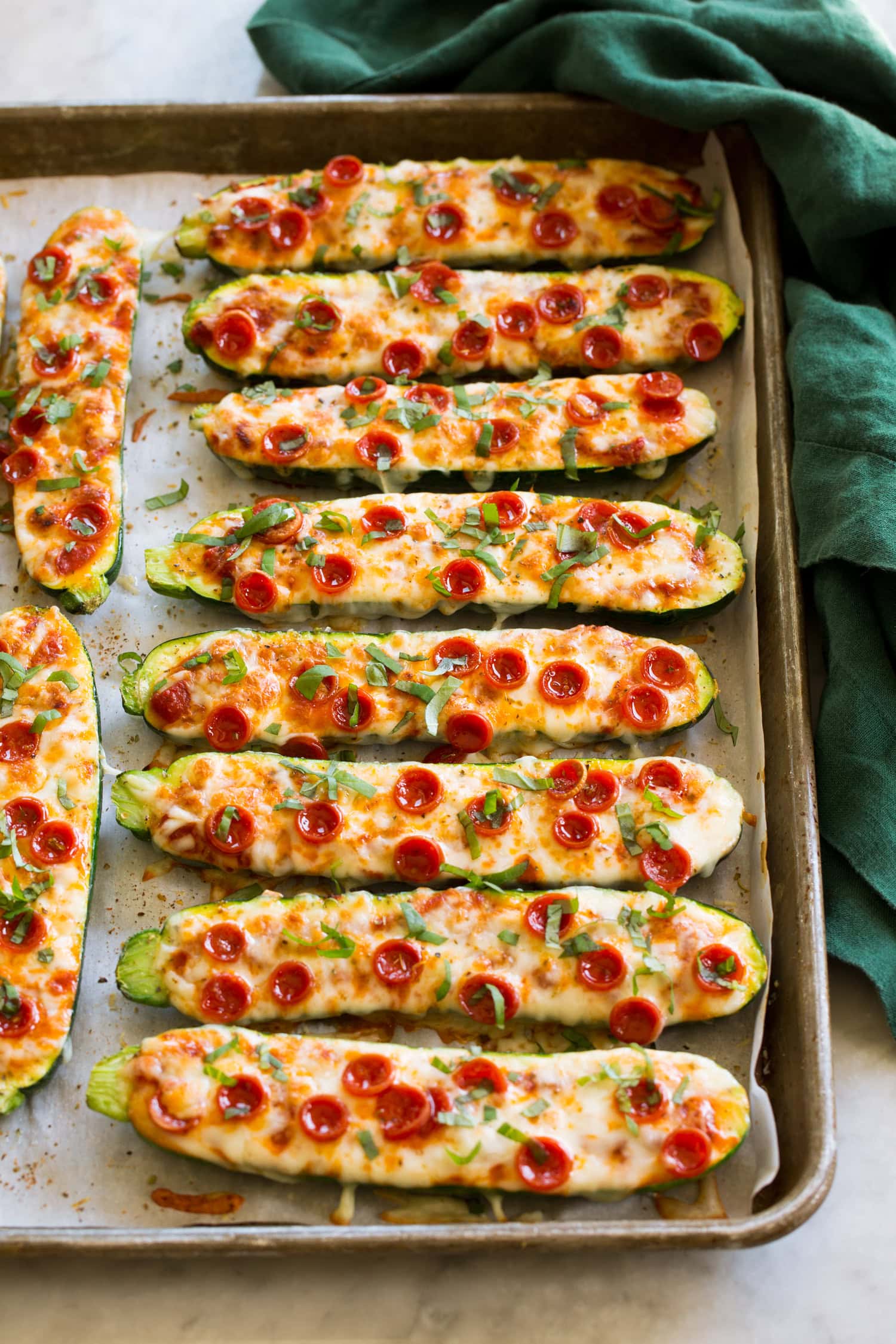 Zucchini Pizza Boats on a large baking sheet with a green cloth to the side.