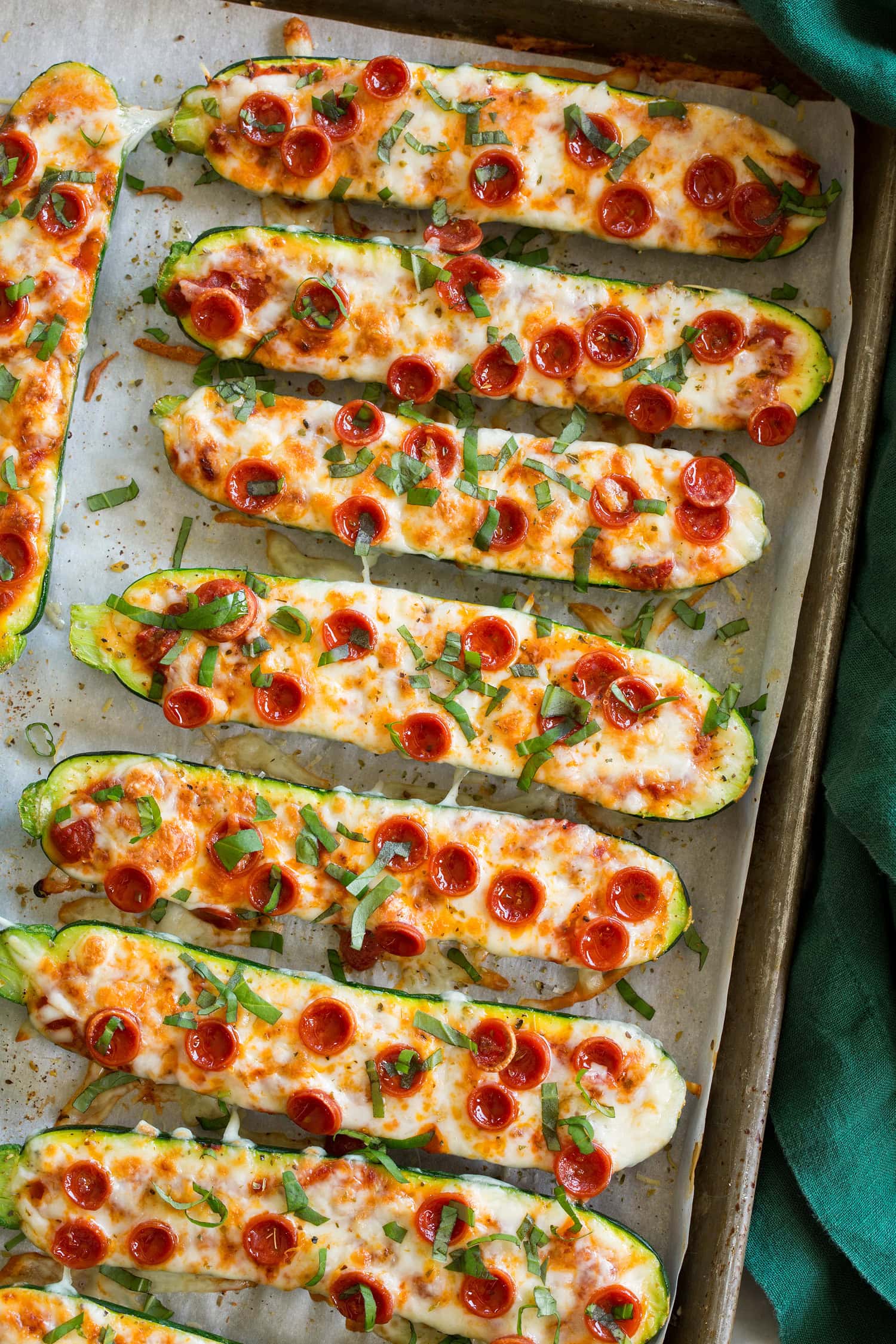 Zucchini halves with melted mozzarella, pizza sauce, pepperoni, and basil on top.